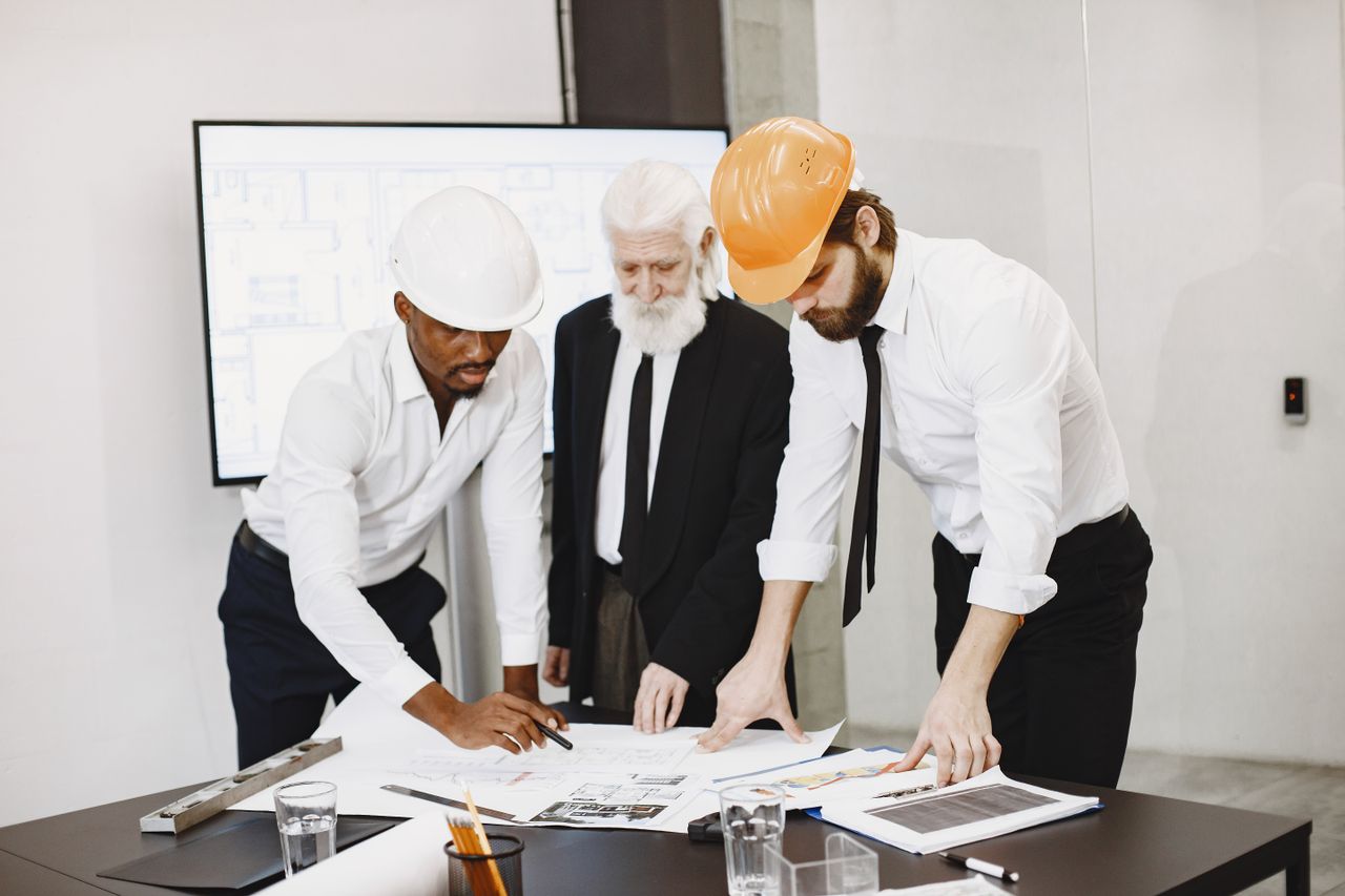 Three professionals in an office setting reviewing building plans and collaborating on a construction project.